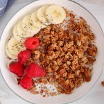 Overhead view on a bowl of sourdough discard granola with milk, banana and raspberries.