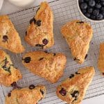 Blueberry sourdough scones on a cooling rack with a side of fresh blueberries.