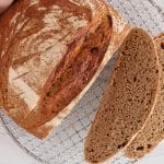 There is a boule of homemade 100% whole wheat bread with a part sliced off to to show the inside crumb.