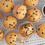 A few vegan sourdough chocolate chip muffins on a cooling rack with 2 of them that have a bite taken off.
