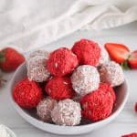 Small plate covered with a pile of healthy strawberry bliss balls with some covered with shredded coconut and others covered with freeze-dried strawberries.