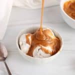 A stream of 3-ingredient peanut butter caramel falling on some vanilla ice cream.