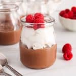 Vegan chocolate cashew mousse in a small jar garnished with whipped cream and raspberries.