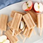 Vegan apple popsicles with yogurt on a white plate with sliced apple on the side.