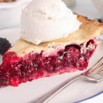 A slice of vegan blackberry pie topped with ice cream and placed on a small plate.
