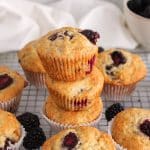 A few blackberry banana muffins piled over each other on a cooling rack.