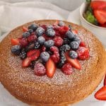 Vegan olive oil cake on a cake platter and garnished with berries.