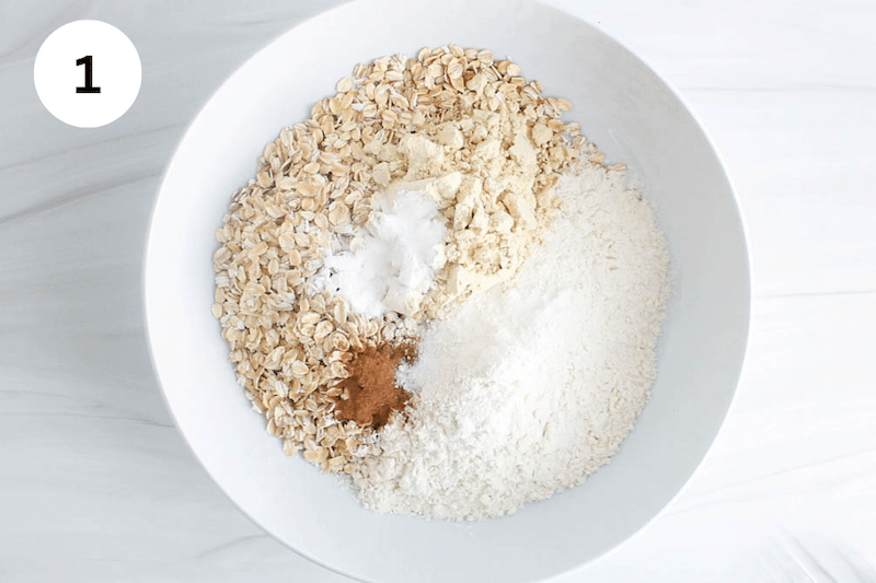 A white bowl with flour, rolled oats, cinnamon and baking powder.