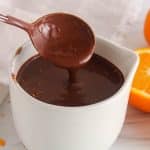 A spoon pouring some dairy-free orange chocolate ganache ion a white pot.