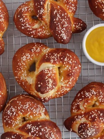A cooling rack filled with large sourdough discard soft pretzel and a mustard sauce.