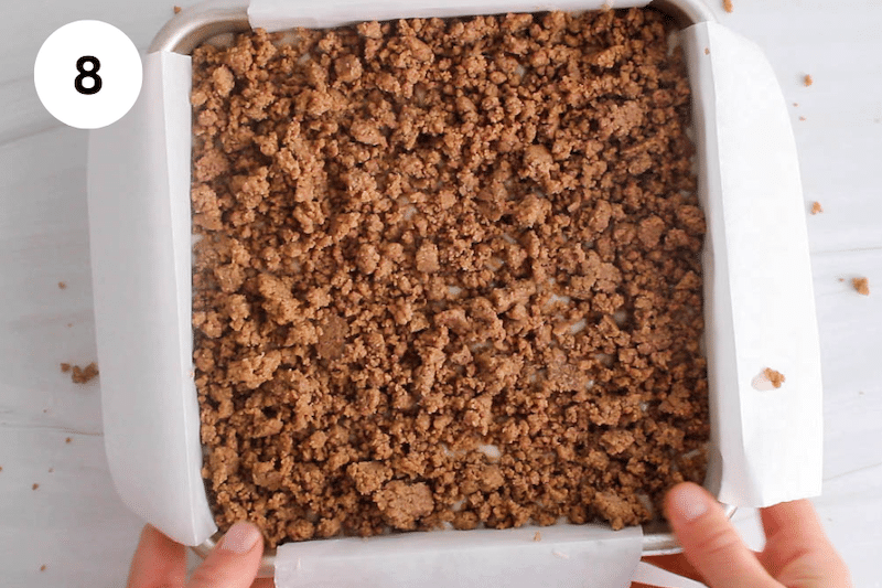 A brownie pan with a coffee cake while hand are picking it up.
