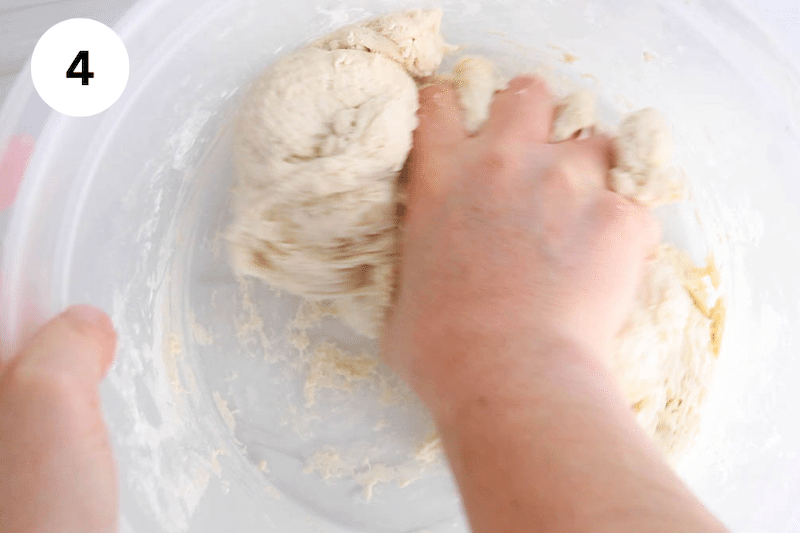 A hand kneading dough in a large container.