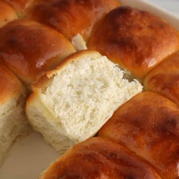 A large dish with sourdough discard rolls and one of the rolls flipped with show the texture of the crumb.