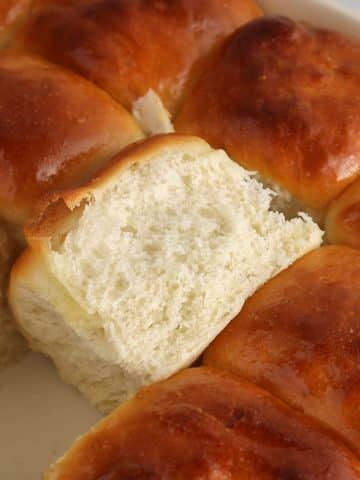 A large dish with sourdough discard rolls and one of the rolls flipped with show the texture of the crumb.