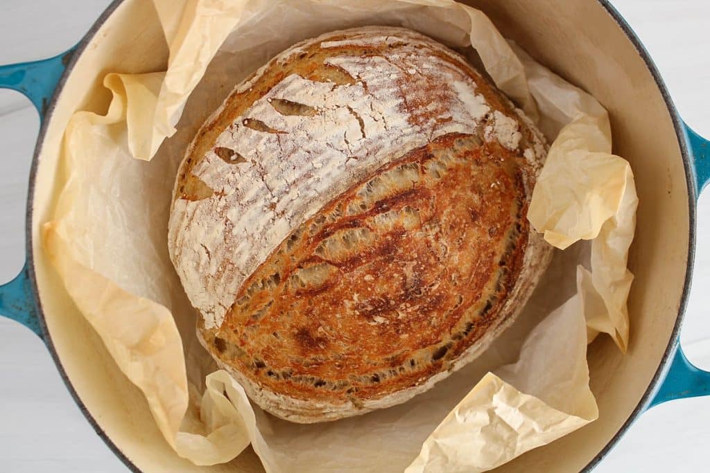 Overhead view on a freshly baked sourdough oatmeal bread in a creuset cast iron baking dish.