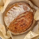 Overhead view on a freshly baked sourdough oatmeal bread in a creuset cast iron baking dish.
