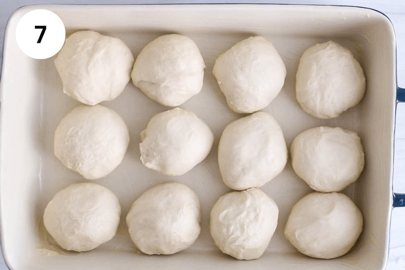 12 small balls of dough on a rectangular greased dish.