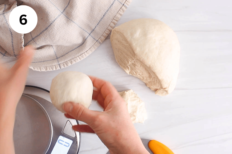 A hand diving a large ball of dough into smaller balls.