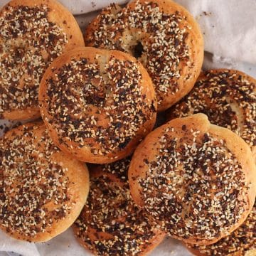 A pile of sourdough discard bagels garnished with everything seasoning and placed on a white cloth.