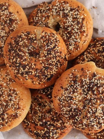 A pile of sourdough discard bagels garnished with everything seasoning and placed on a white cloth.