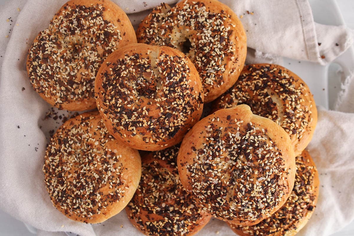 A pile of sourdough discard bagels garnished with everything seasoning and placed on a white cloth.