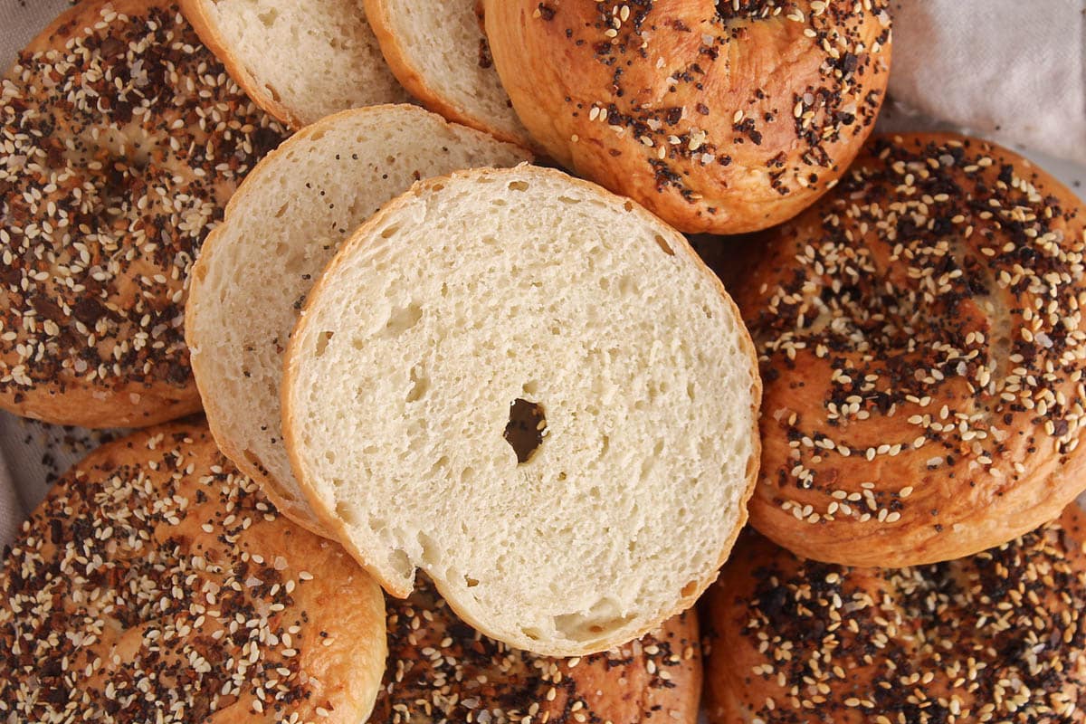 A sliced sourdough discard bagels on a pile of everything bagels.