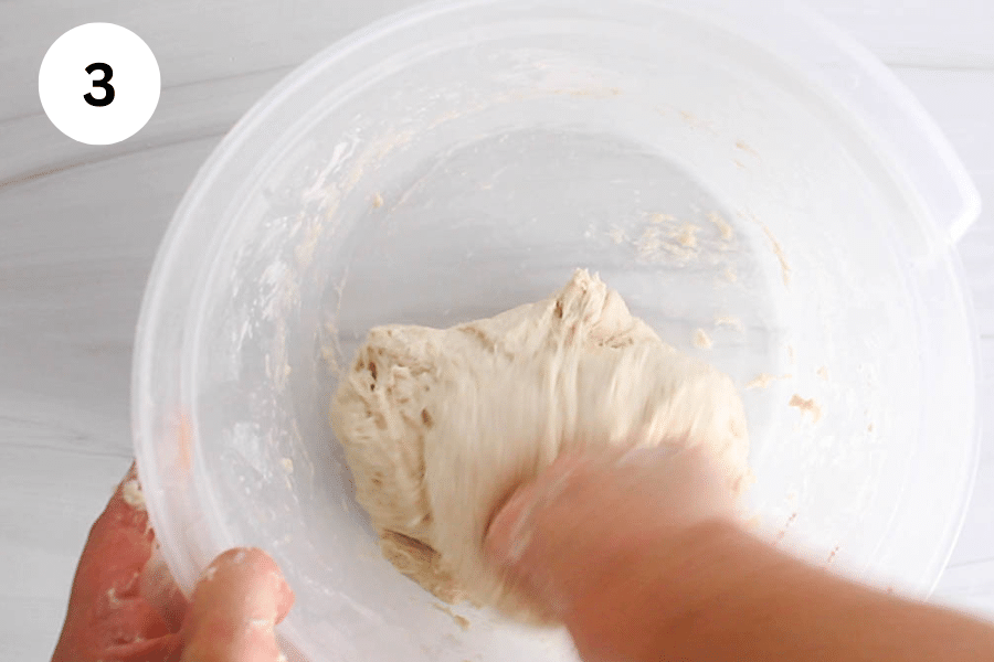 A hand mixing a dough in a large container.