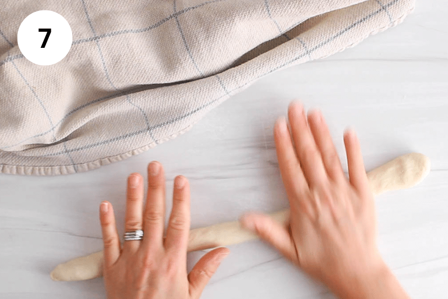 A hand rolling some dough into a long tube.