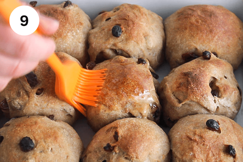 A brush brushing melted butter over baked buns.