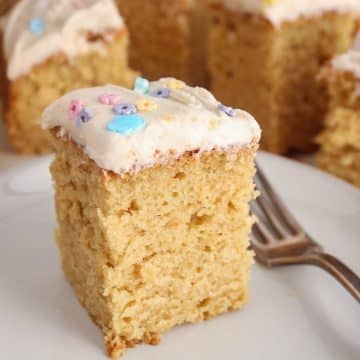 A square of vegan vanilla sourdough cake with a vanilla frosting on a plate with a fork.