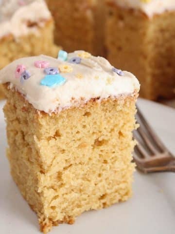 A square of vegan vanilla sourdough cake with a vanilla frosting on a plate with a fork.