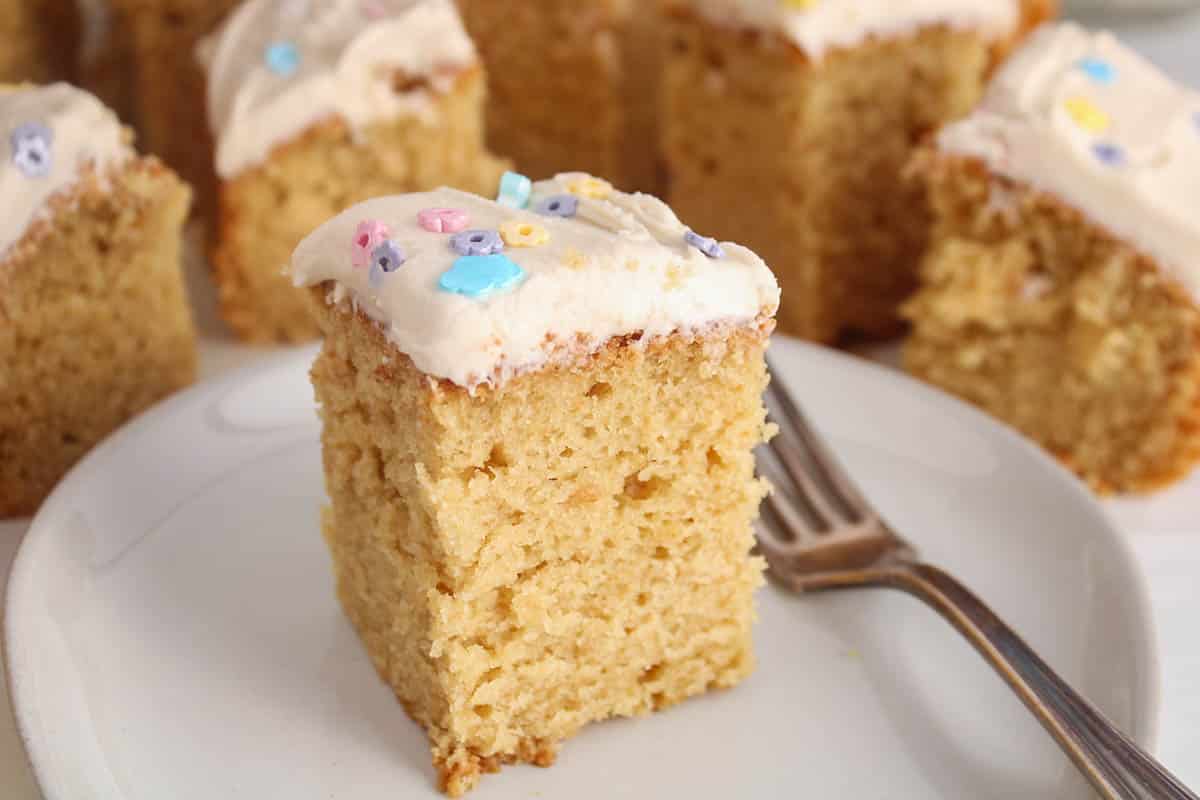 A square of vegan vanilla sourdough cake with a vanilla frosting on a plate with a fork.