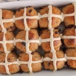 Vegan sourdough hot cross buns with raisin and covered with icing in a large white baking dish.
