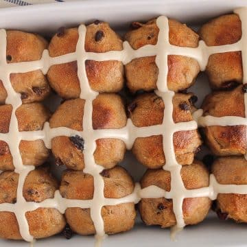 Vegan sourdough hot cross buns with raisin and covered with icing in a large white baking dish.
