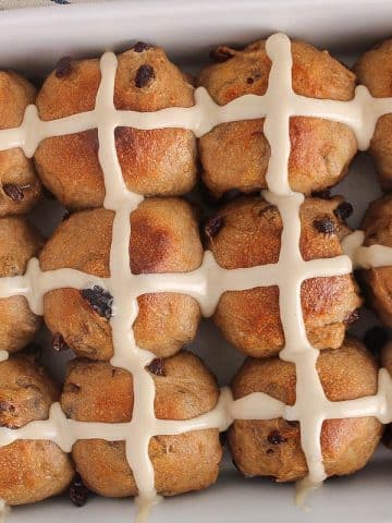 Vegan sourdough hot cross buns with raisin and covered with icing in a large white baking dish.