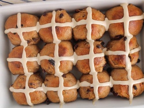 Vegan sourdough hot cross buns with raisin and covered with icing in a large white baking dish.