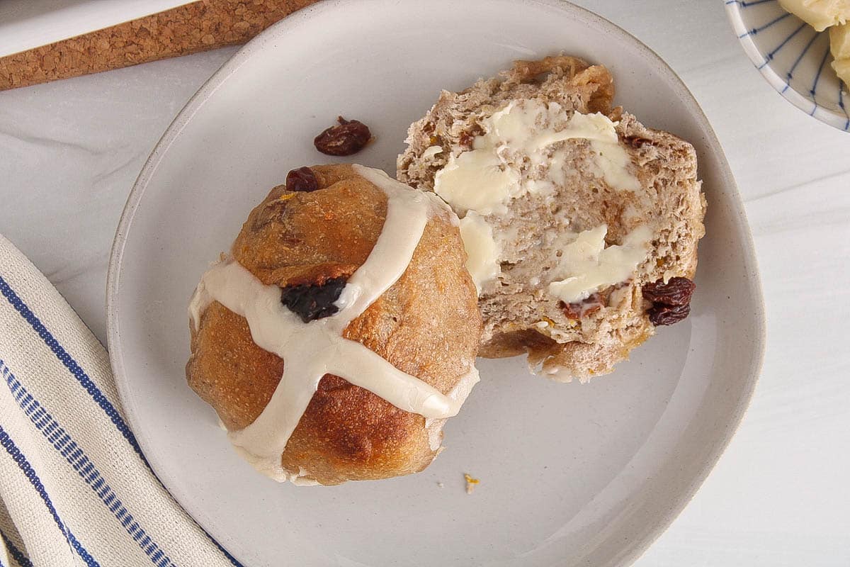 A sourdough hot cross bun sliced in half and covered with butter.