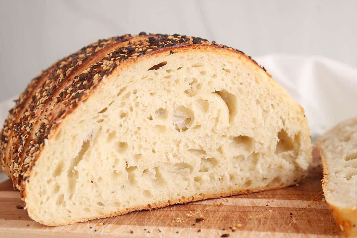 A half sliced everything bagel sourdough bread on a cutting board showing its interior crumb.