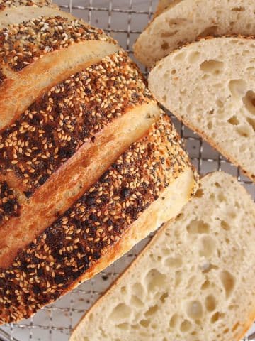 A half sliced loaf of everything bagel sourdough bread placed on a cooling rack.