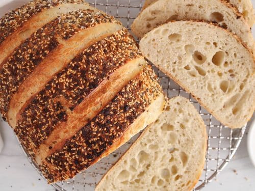 A half sliced loaf of everything bagel sourdough bread placed on a cooling rack.
