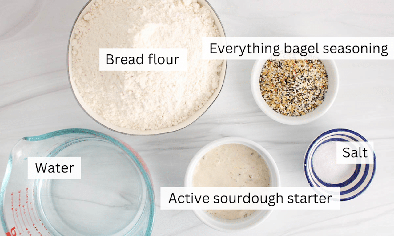 Showing are the ingredients needed to make everything bagel sourdough bread placed on a table.