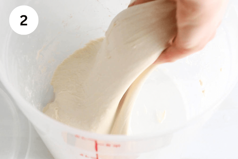 Hand stretching dough from a bowl.