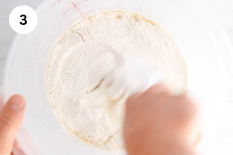 A whisk stirring in a container with the dough ingredients.
