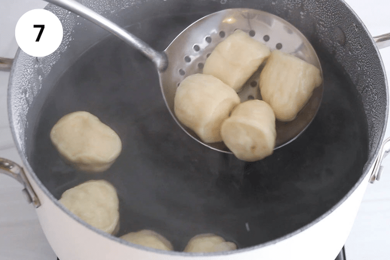 A large slotted spoon taking some small balls of dough from a large pot of boiling water.