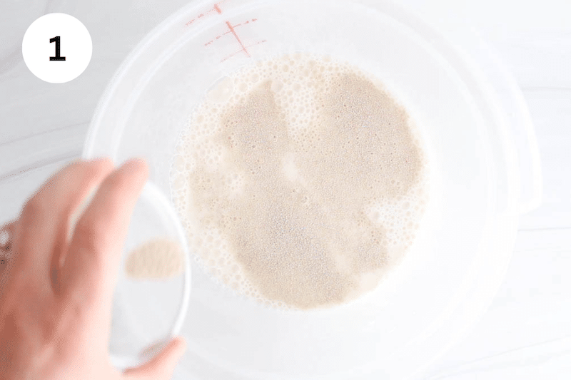A large container with liquidy ingredient and a small bowl sprinkling some dry active yeast.
