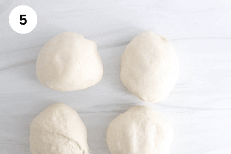 4 large balls of dough on a counter.