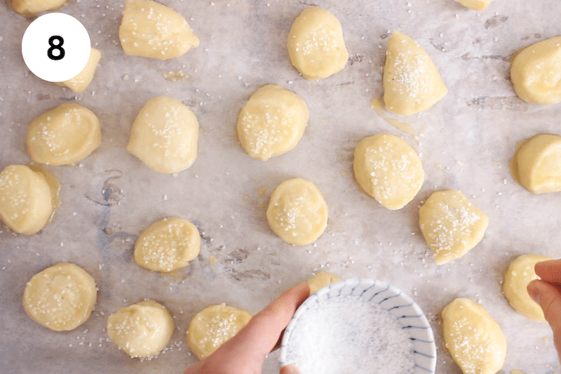 Hands sprinkling pretzel salt over the bites.