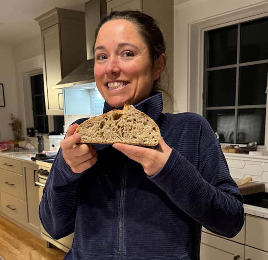 Jess is holding a halved sliced loaf of bread in her kitchen.