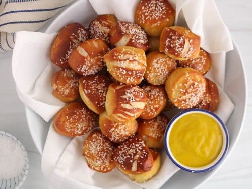 Sourdough discard pretzel bites in a white bowl with a mustard sauce.