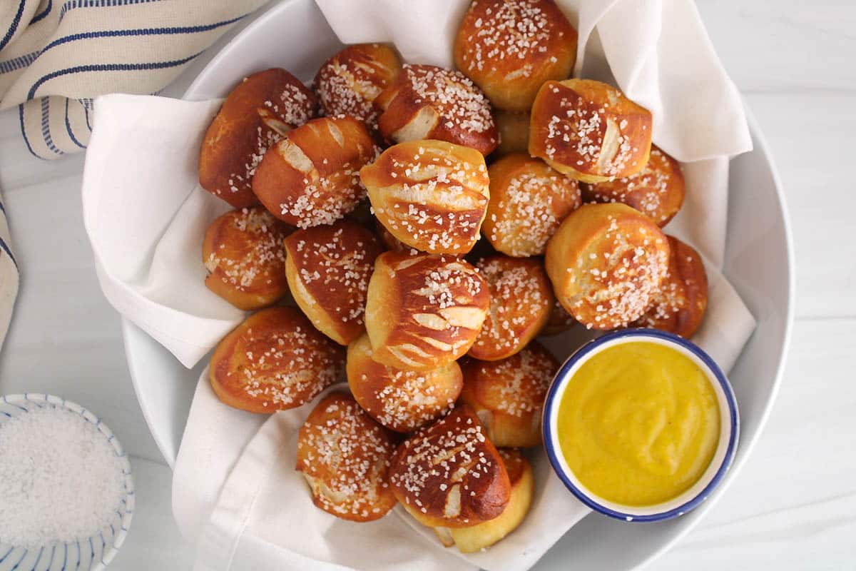 Sourdough discard pretzel bites in a white bowl with a mustard sauce.